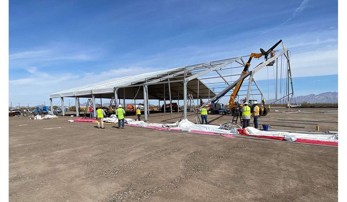 A group of construction workers in safety apparel assembling a temporary fabric structure at a job site.