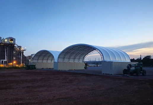An industrial facility with two large temporary structures at dusk.