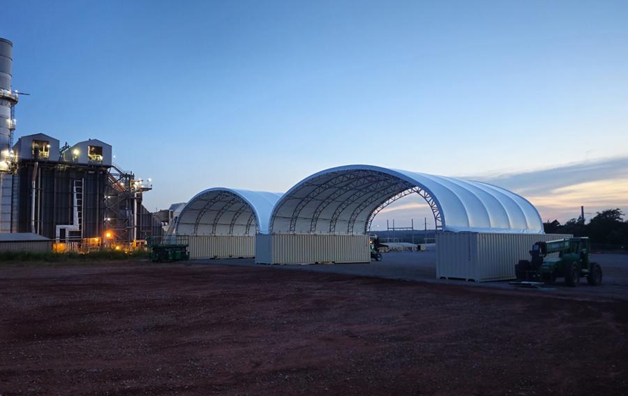 An industrial facility with two large temporary structures at dusk.
