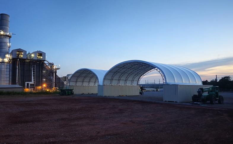 An industrial facility with two large temporary structures at dusk.
