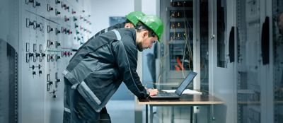 People standing at a table, recording generator testing results on laptop computers.