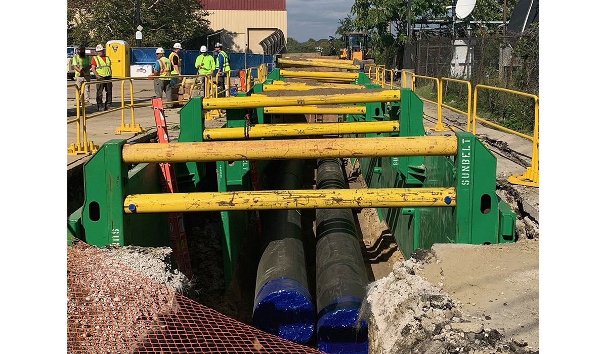 Construction crew installing large underground pipelines within a supported trench.