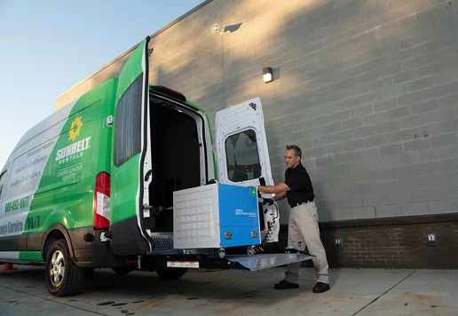 Someone unloading an air scrubber from a Sunbelt Rentals van.