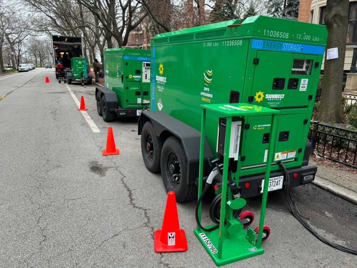 Several Sunbelt Rentals BESS units parked along a street, surrounded by orange safety cones.