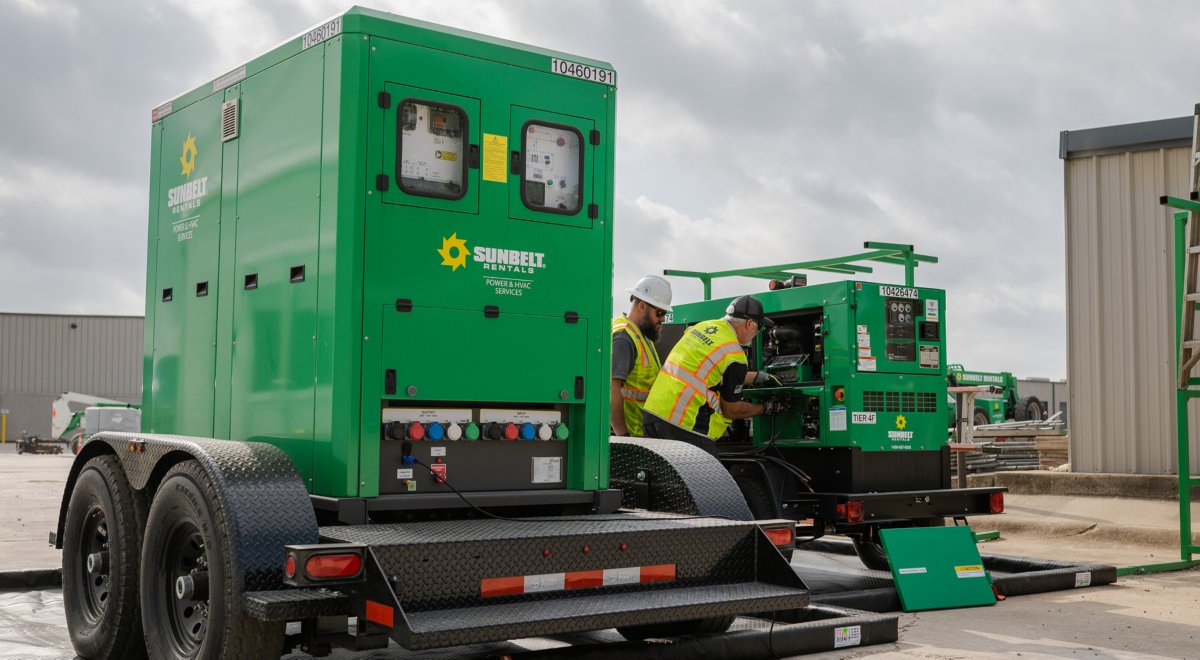 Two workers in safety apparel inspecting Sunbelt Rentals BESS units outdoors.