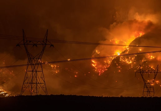 A large wildfire on a hillside surrounded by power lines.