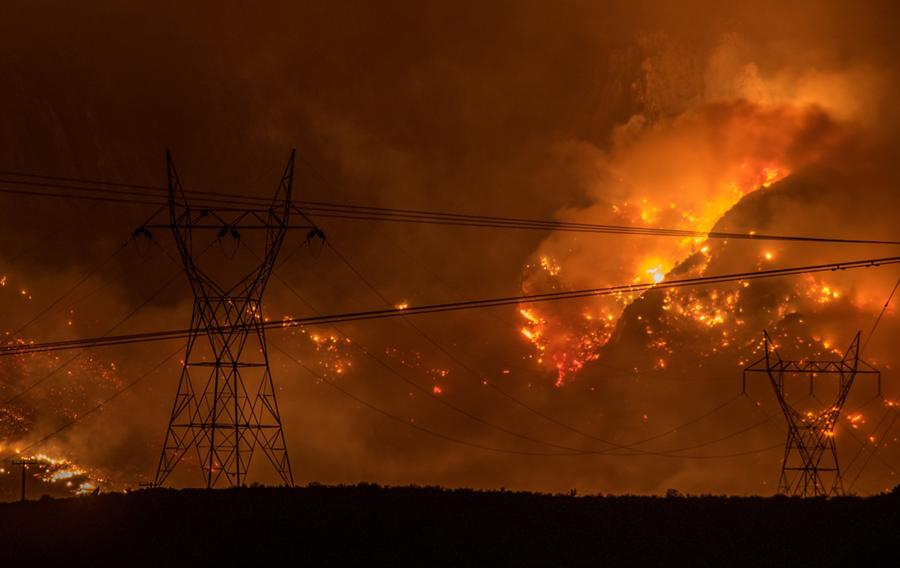 A large wildfire on a hillside surrounded by power lines.