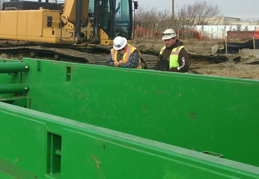 Construction workers inspect large green trench box.