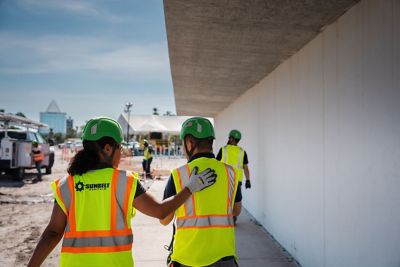 Workers wearing Sunbelt Rentals safety apparel, walking at a job site.